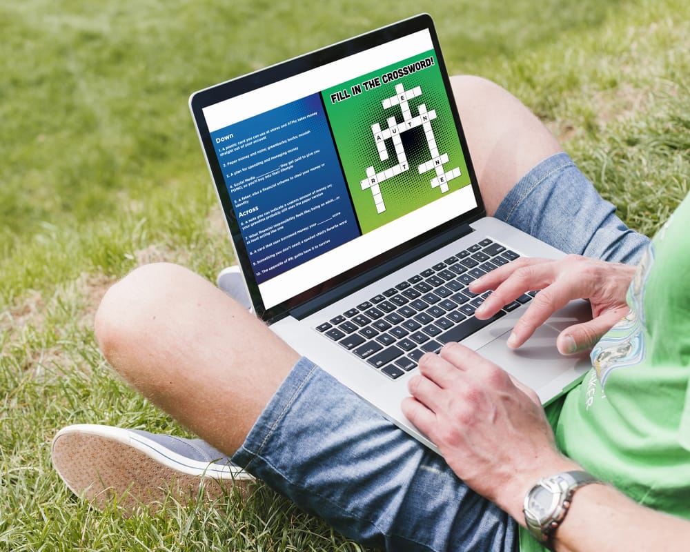 Laptop showing an interactive financial crossword puzzle with blue and green background and clues listed to the side.